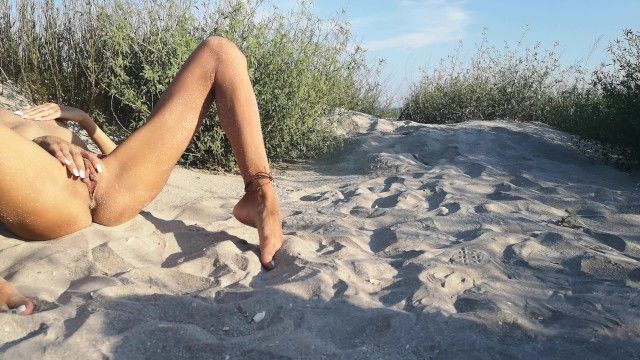法国裸体主义者法定年龄的少年躲在沙滩上，玩着她晒黑的细长身体